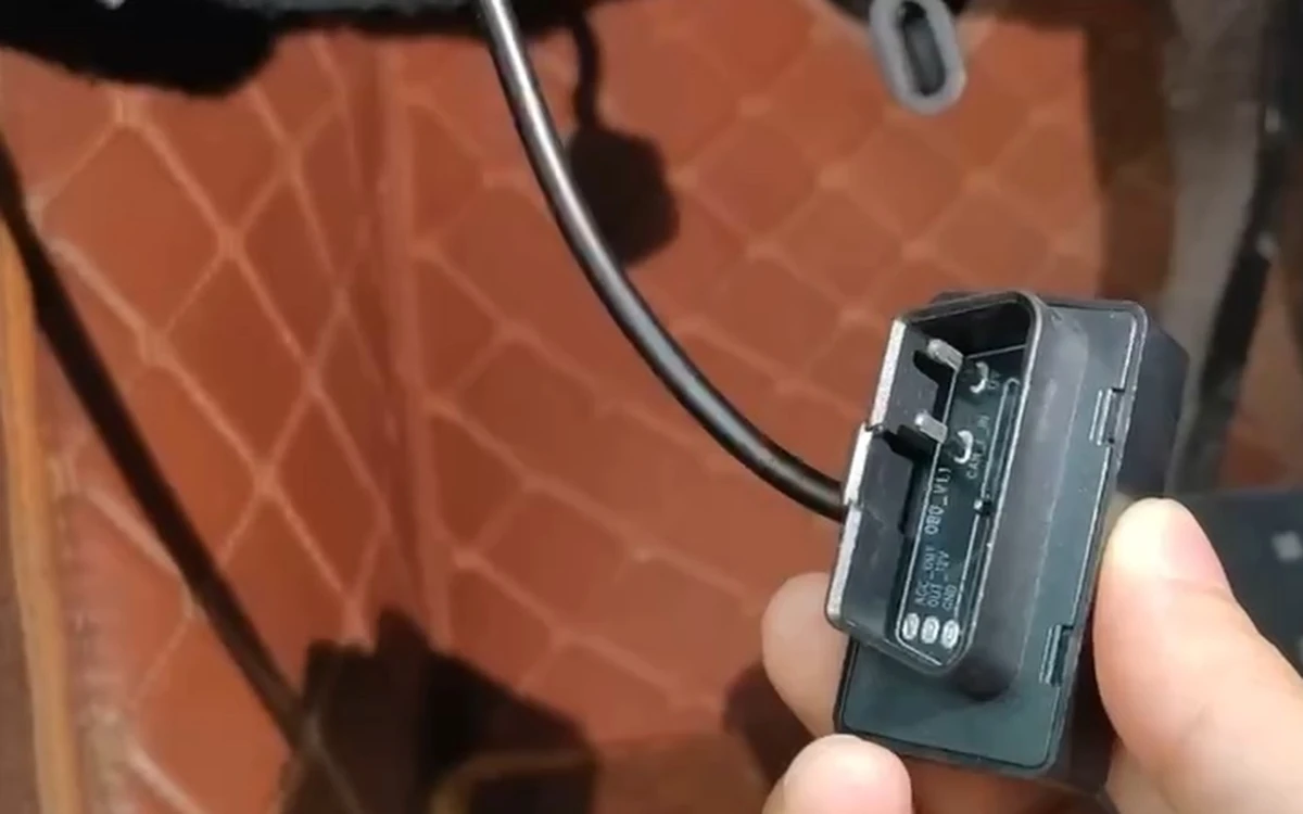 The OBD-II adapter in hand, its 16-pin connector facing the camera